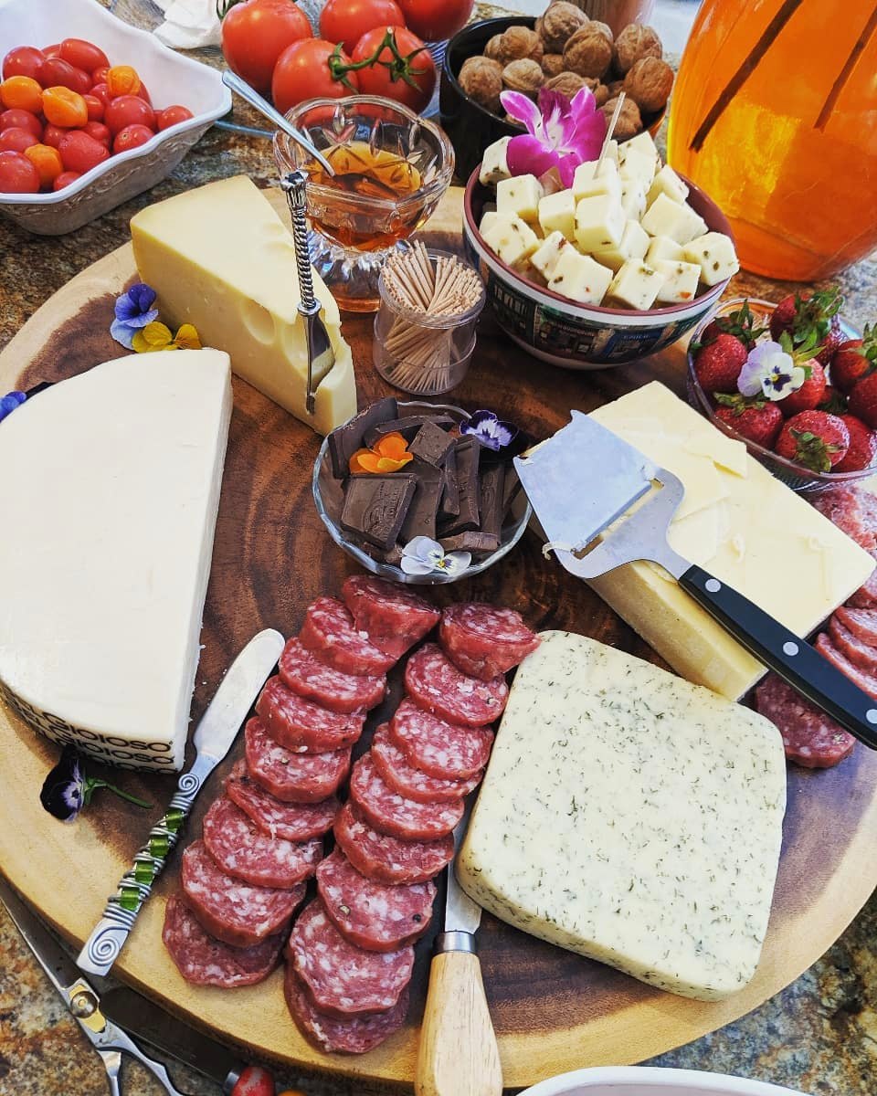 A wooden charcuterie board with cured meats, cheeses, olives and breadsticks