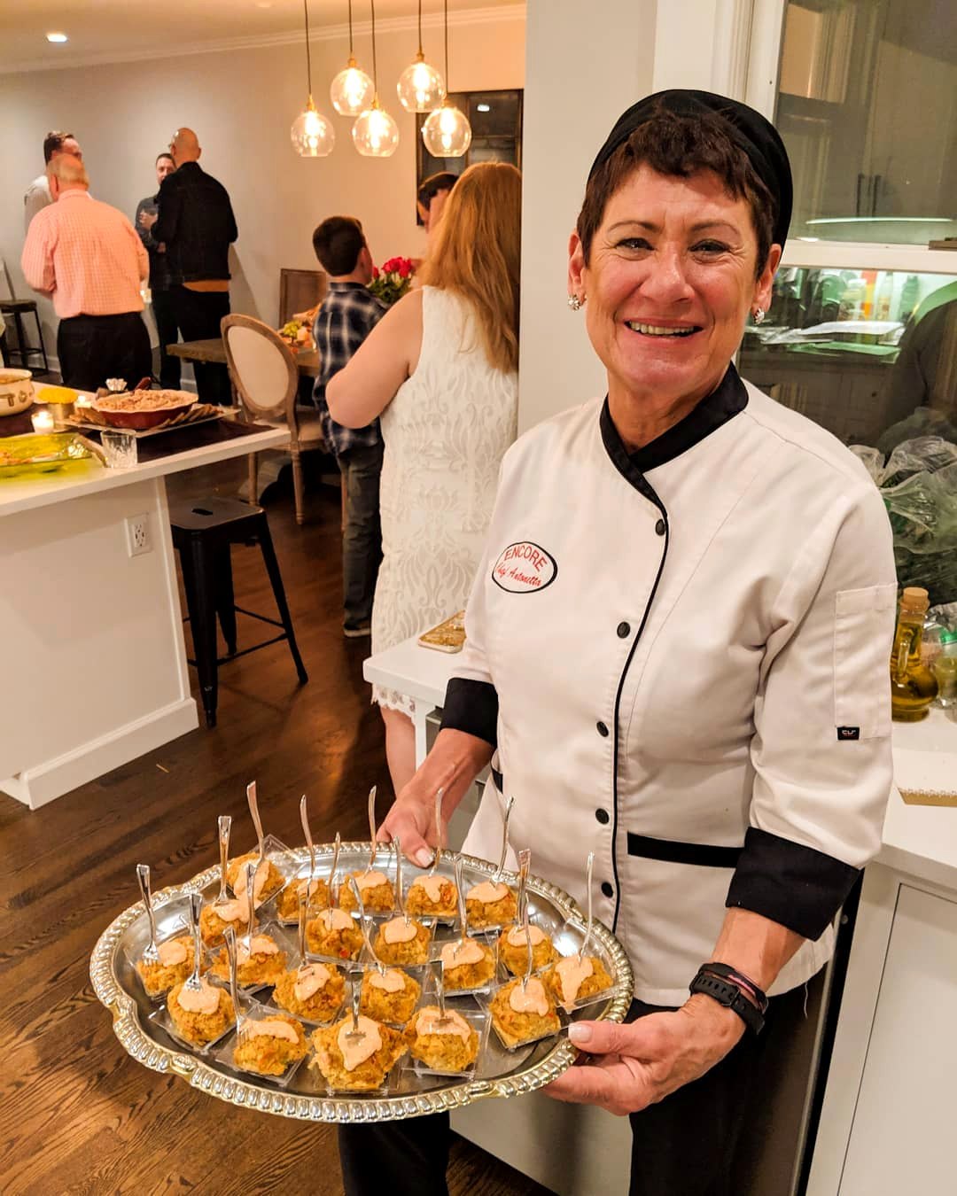 Chef Antoinette in her whites, smiling and holding a platter of crab cake appetizers