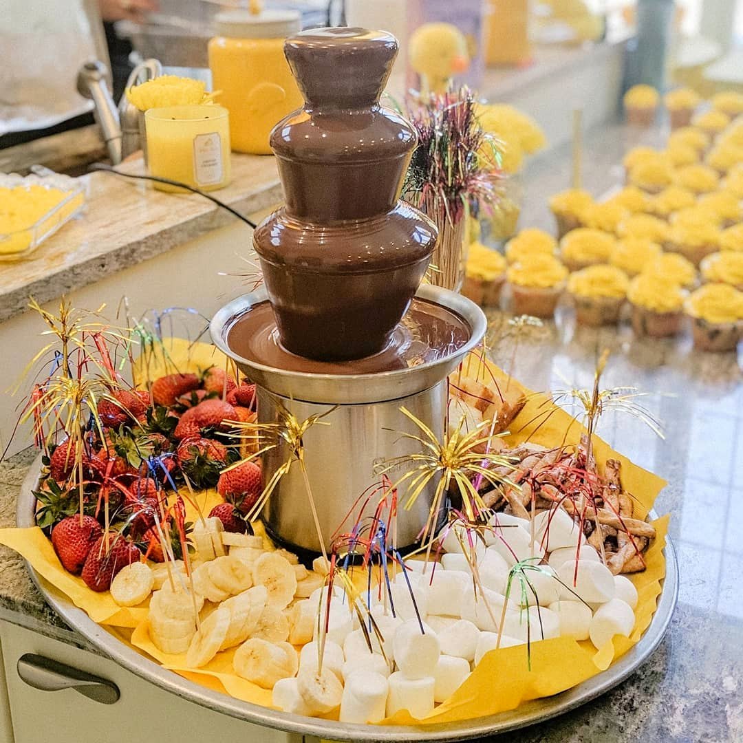 A chocolate fountain surrounded by a platter of fresh fruit skewers