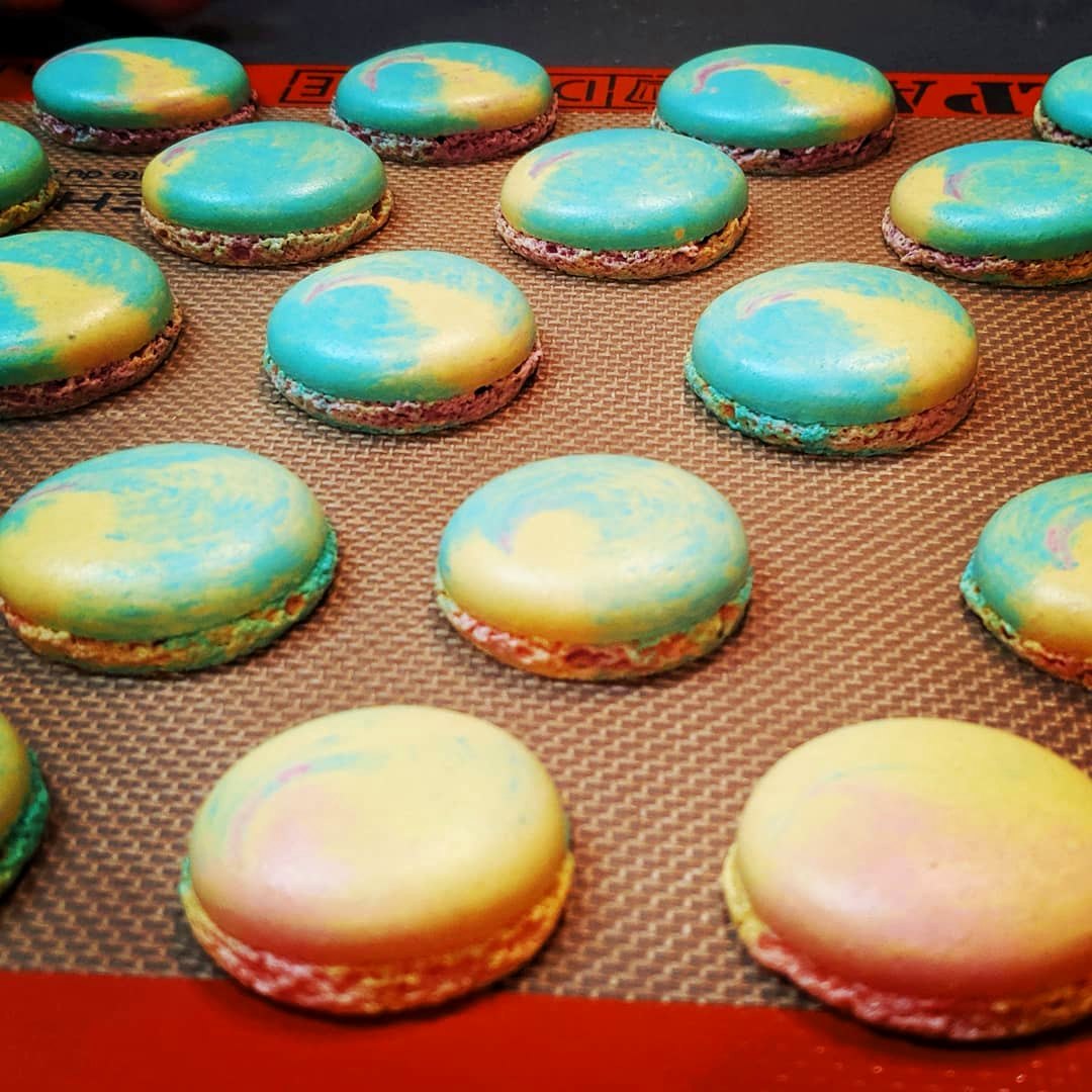 Rows of pastel tye-dye French macarons cooling on a tray