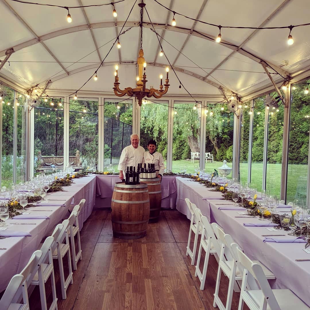 A long table set with white linens under a tented pavilion with chandeliers